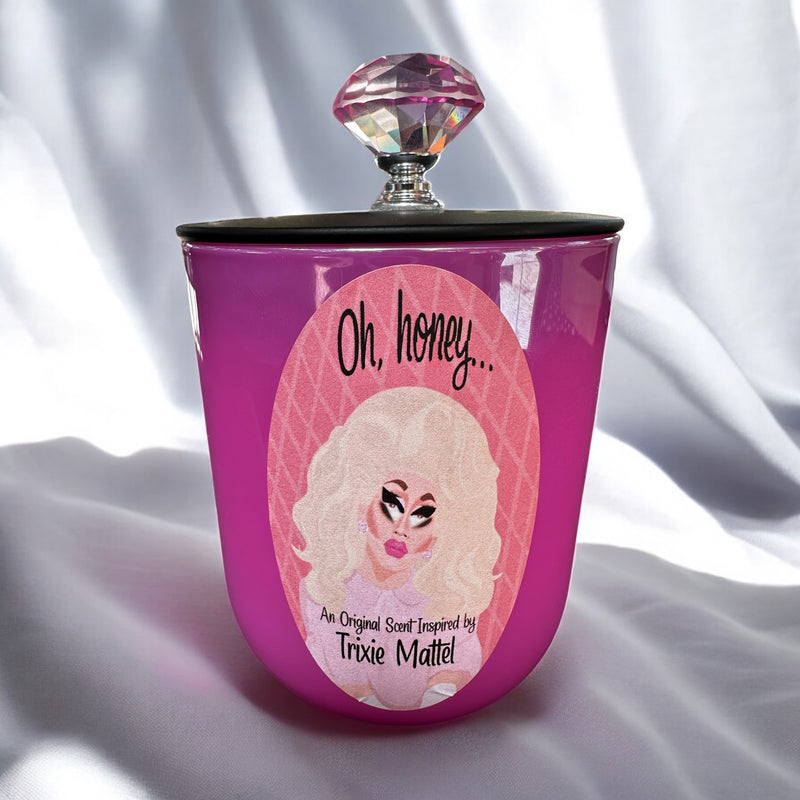 Pink candle with a decorative lid featuring Trixie Mattel and “Oh Honey” text on a white fabric background
