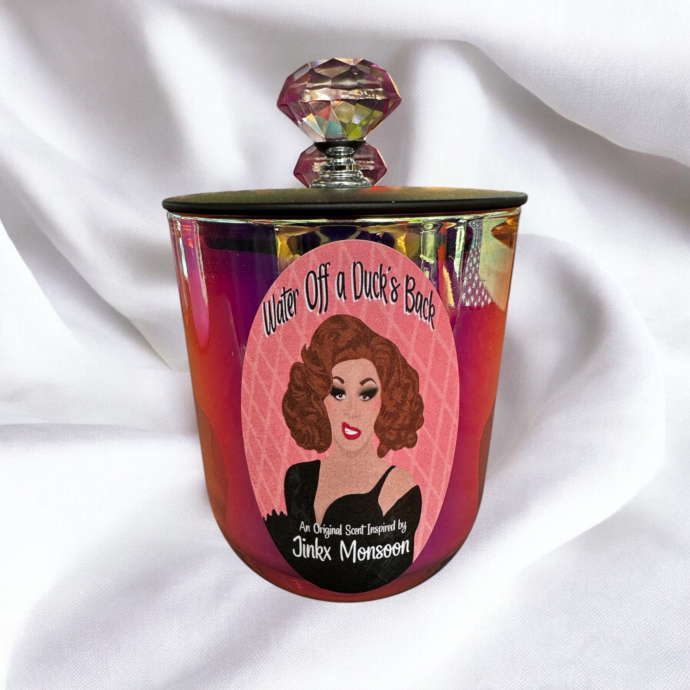 Pink candle with colorful cap and label featuring Jinkx Monsoon on a white fabric background
