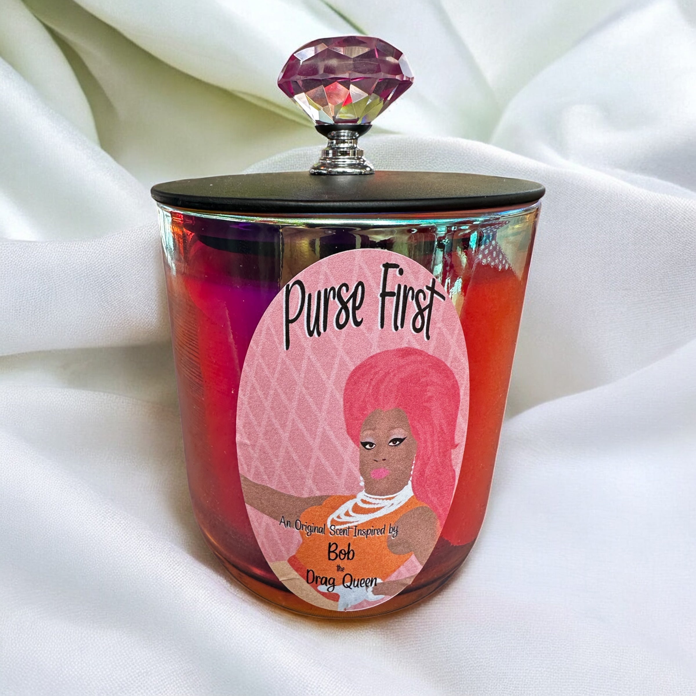 Candle jar with a decorative label featuring Bob the Drag Queen and text on a white fabric background
