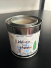 A candle with a label that reads 'Welcome to Our Home, Please Leave by 9', with an illustration of a house and trees.