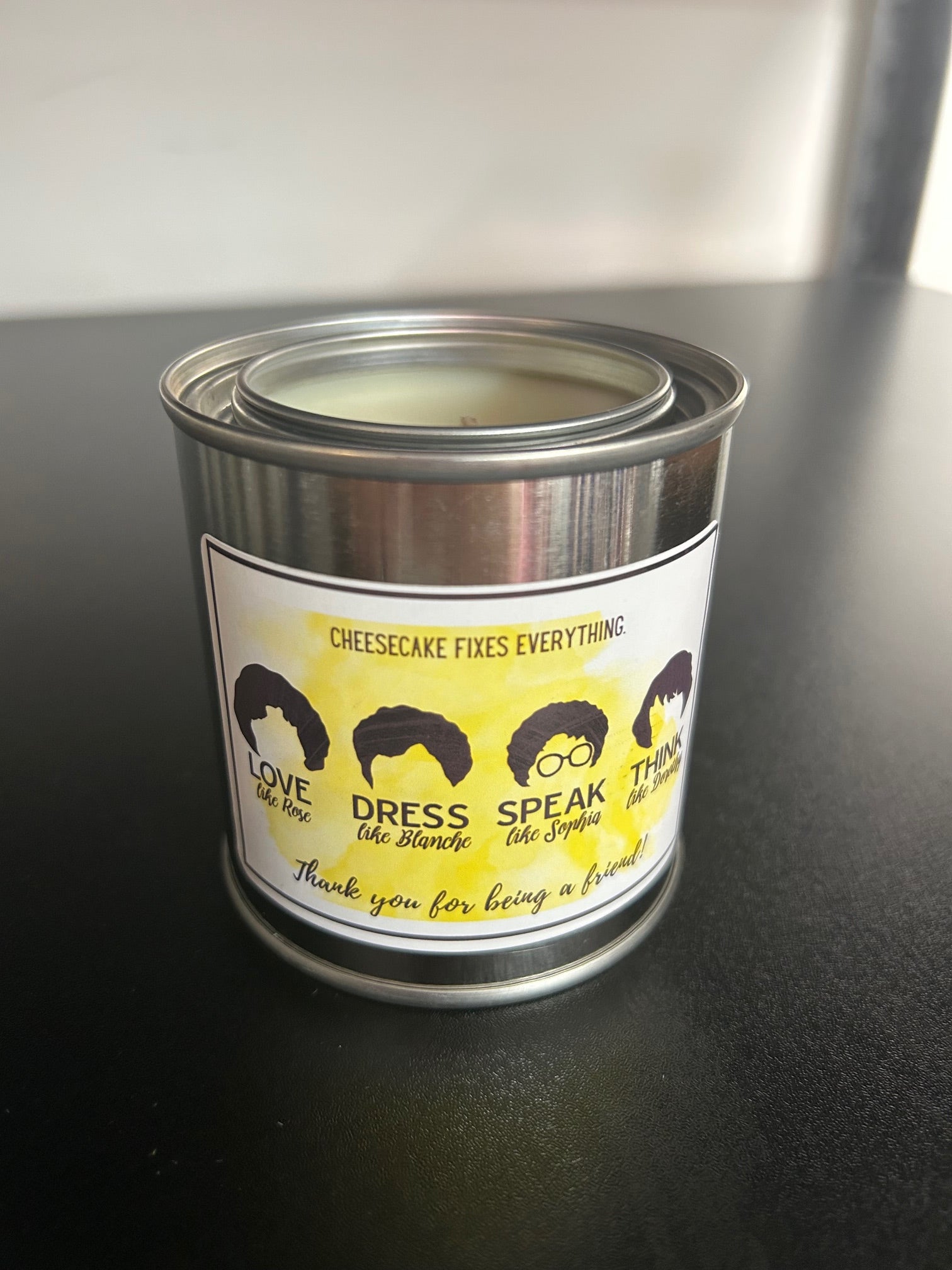 A candle with a label that reads 'Cheesecake Fixes Everything' and has various political and social statements.