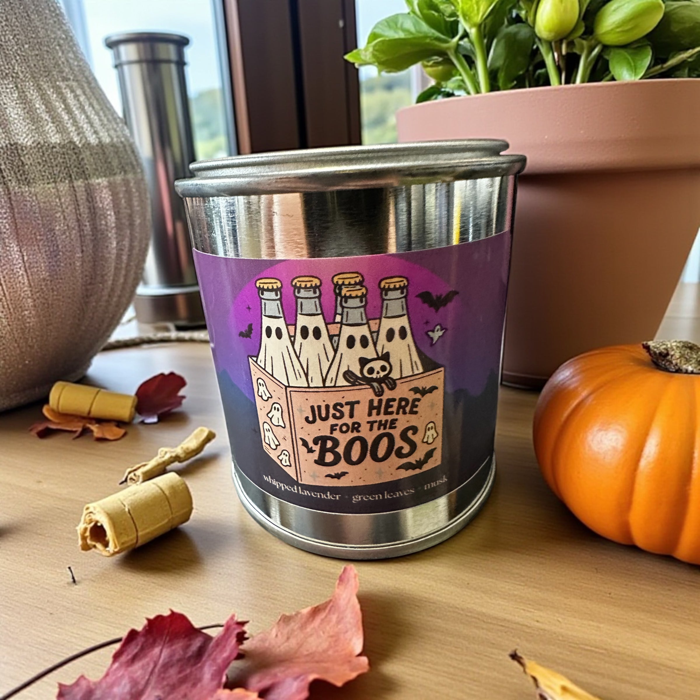 Stainless steel candle with Halloween-themed label on a wooden surface with decorative items.