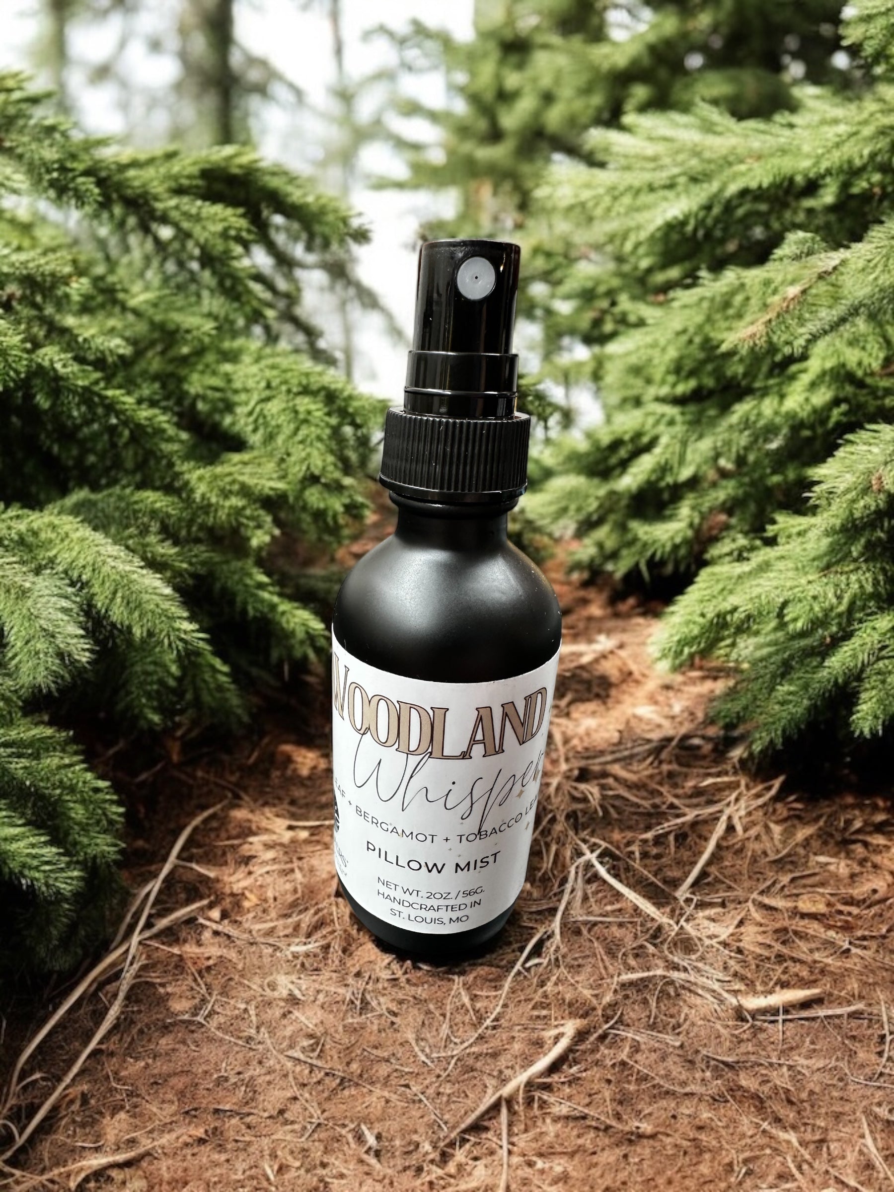 A bottle of Woodland Whisper room spray placed among pine trees.