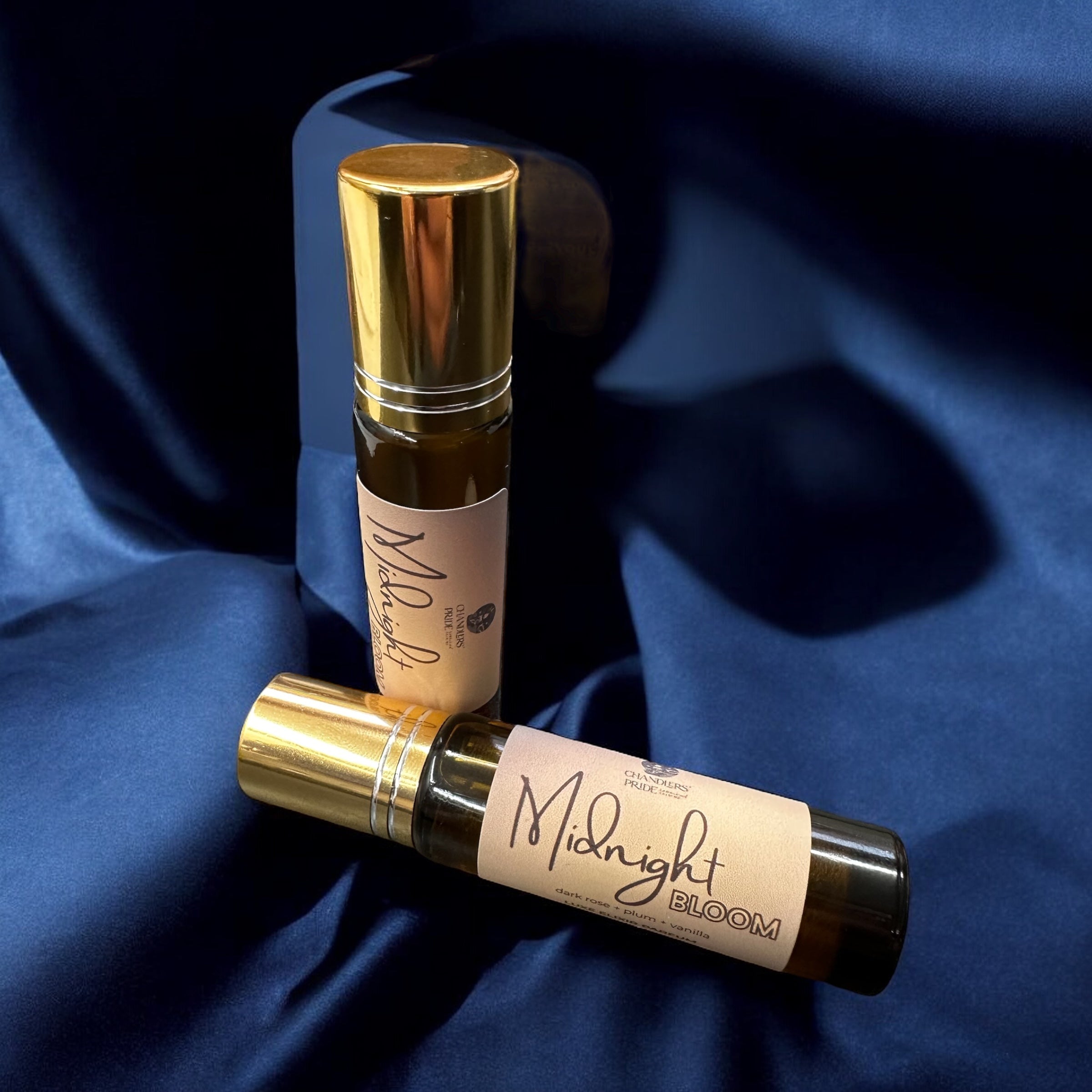 Two rollerball bottles labeled 'Midnight Bloom' on a blue fabric background