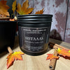 Candle labeled 'SISTAAAS' with autumn leaves and cinnamon sticks on a wooden surface