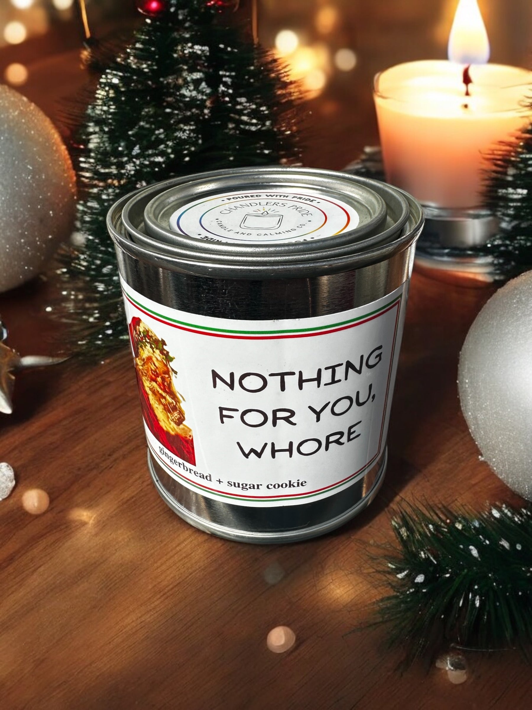 A tin can candle with a label that reads 'Nothing for you, W***e!' and a small picture of a woman. The can is decorated with Christmas-themed decorations around it.