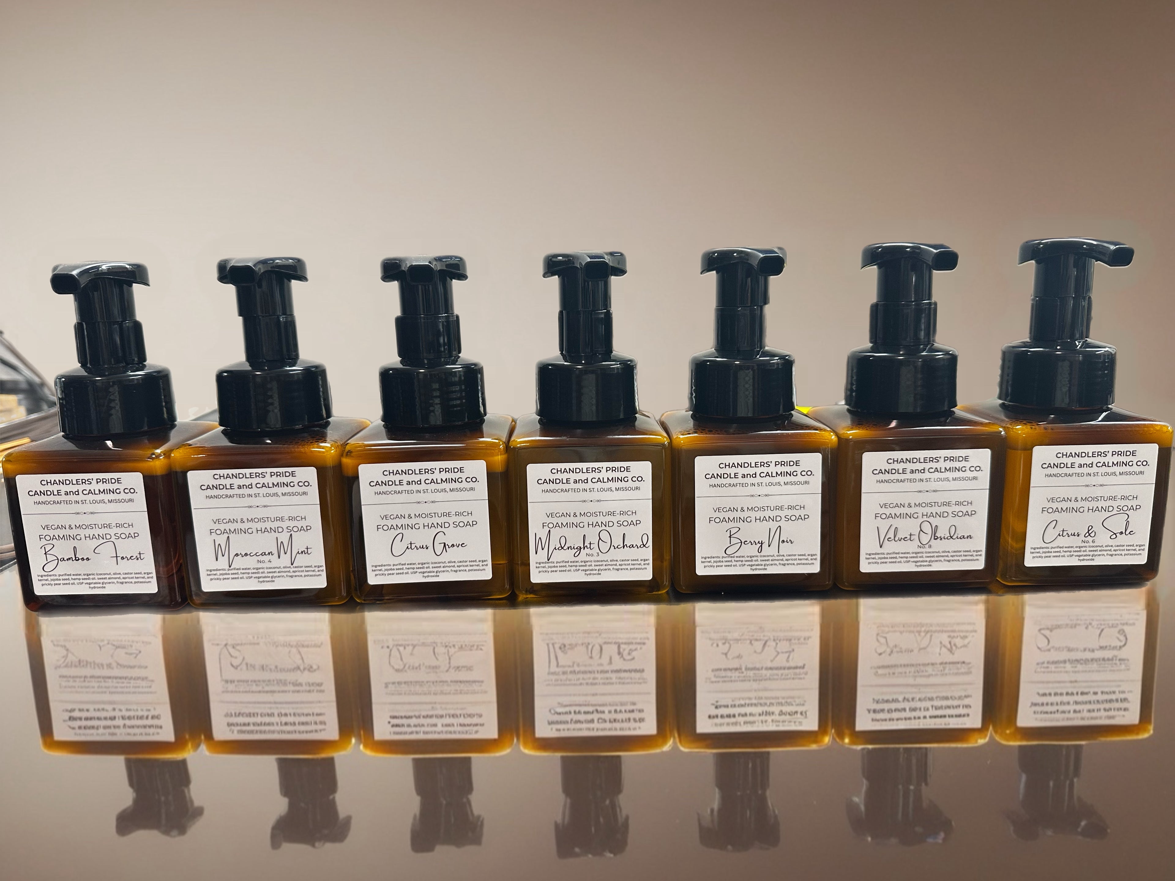 Row of moisture-rich foaming hand soap in brown bottles with black pumps on a reflective surface.