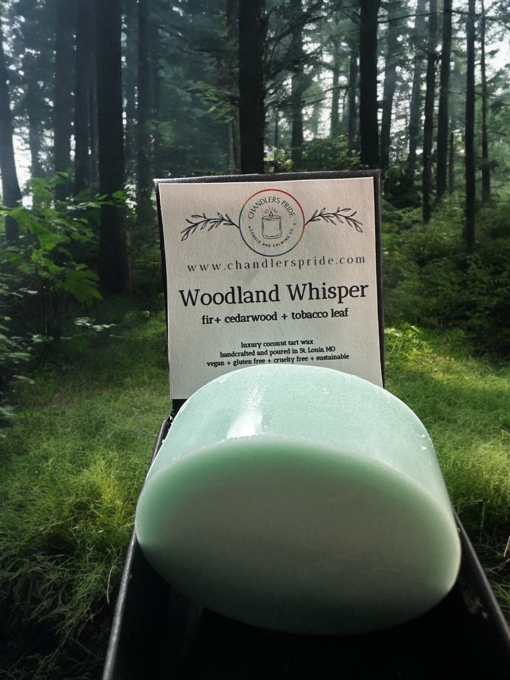 A jar candle with the label 'Woodland Whisper' set on a wooden surface with a backdrop of a serene outdoor scene at sunset.