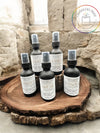 Multiple bottles of Aire Care + Linen spray arranged on a wooden disc with a stone wall in the background.