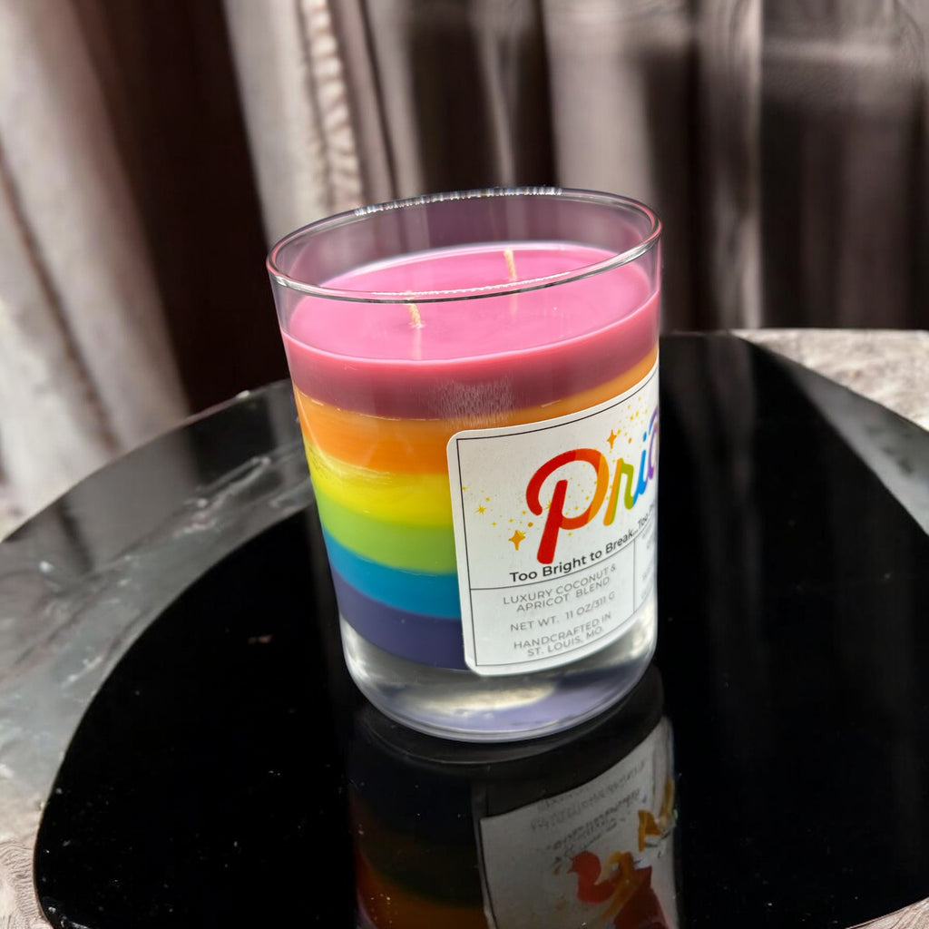 Colorful candle with a rainbow design and a label on a black surface.