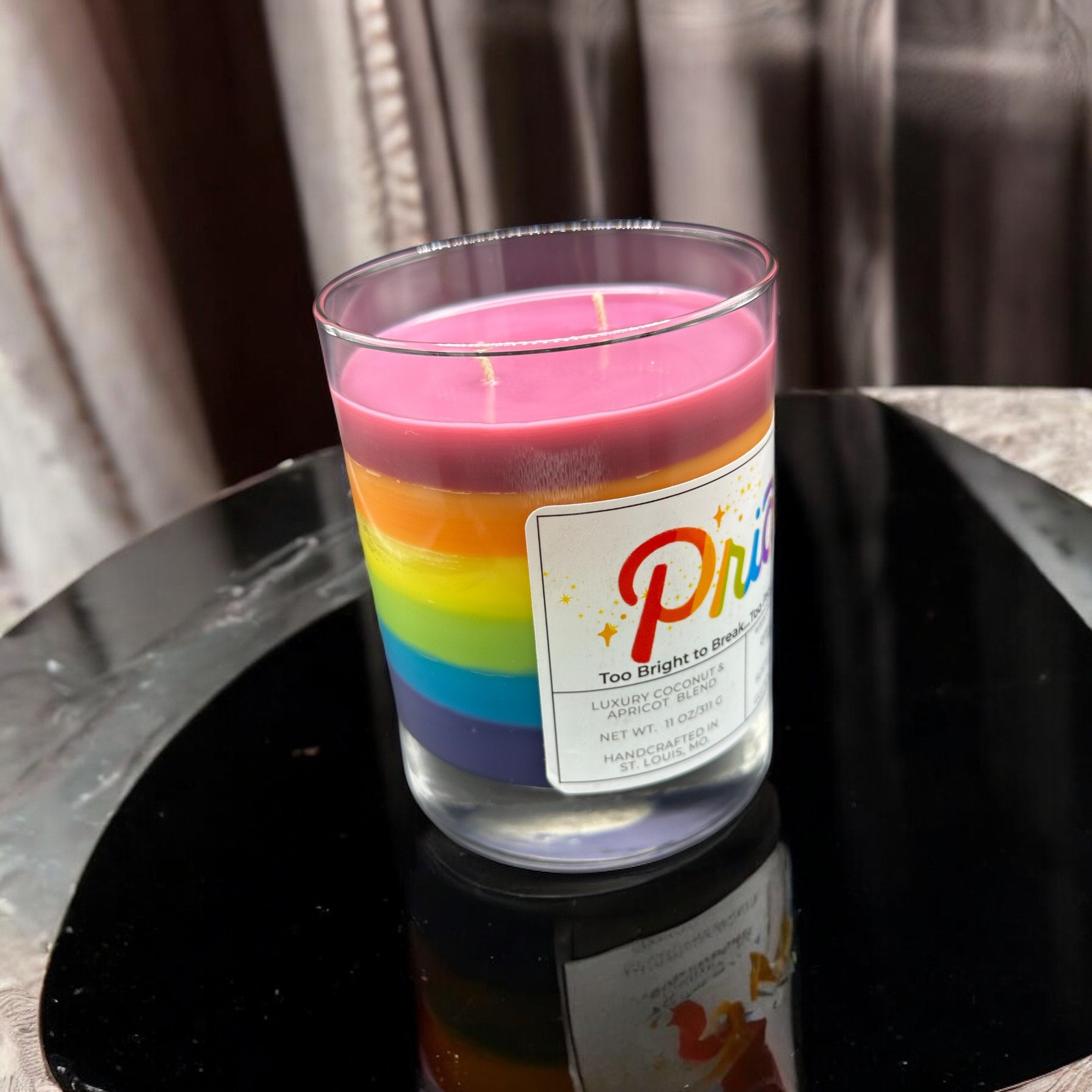 Colorful candle with a rainbow design and a label on a black surface.