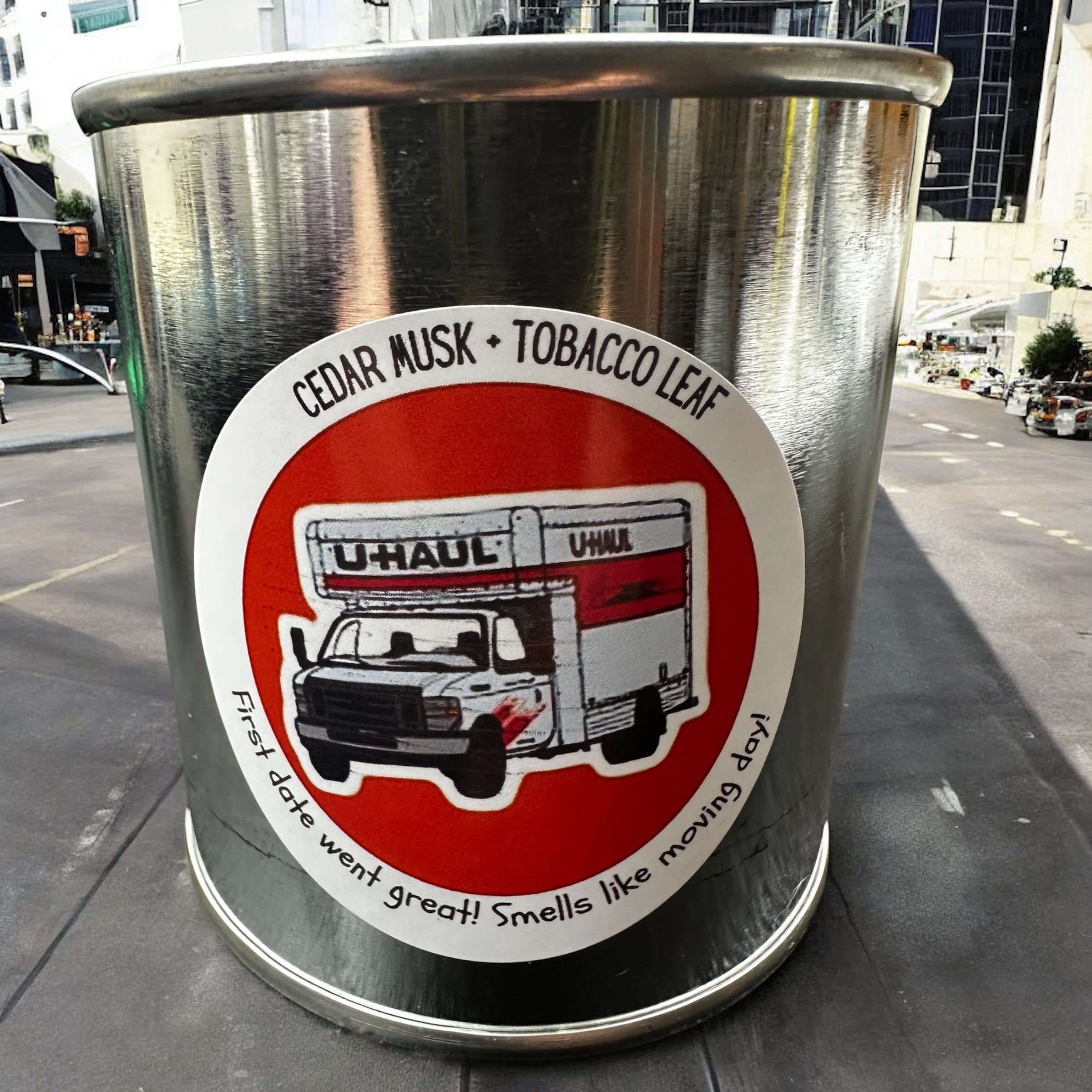 Metal canister with U-Haul truck graphic and text on a city street background