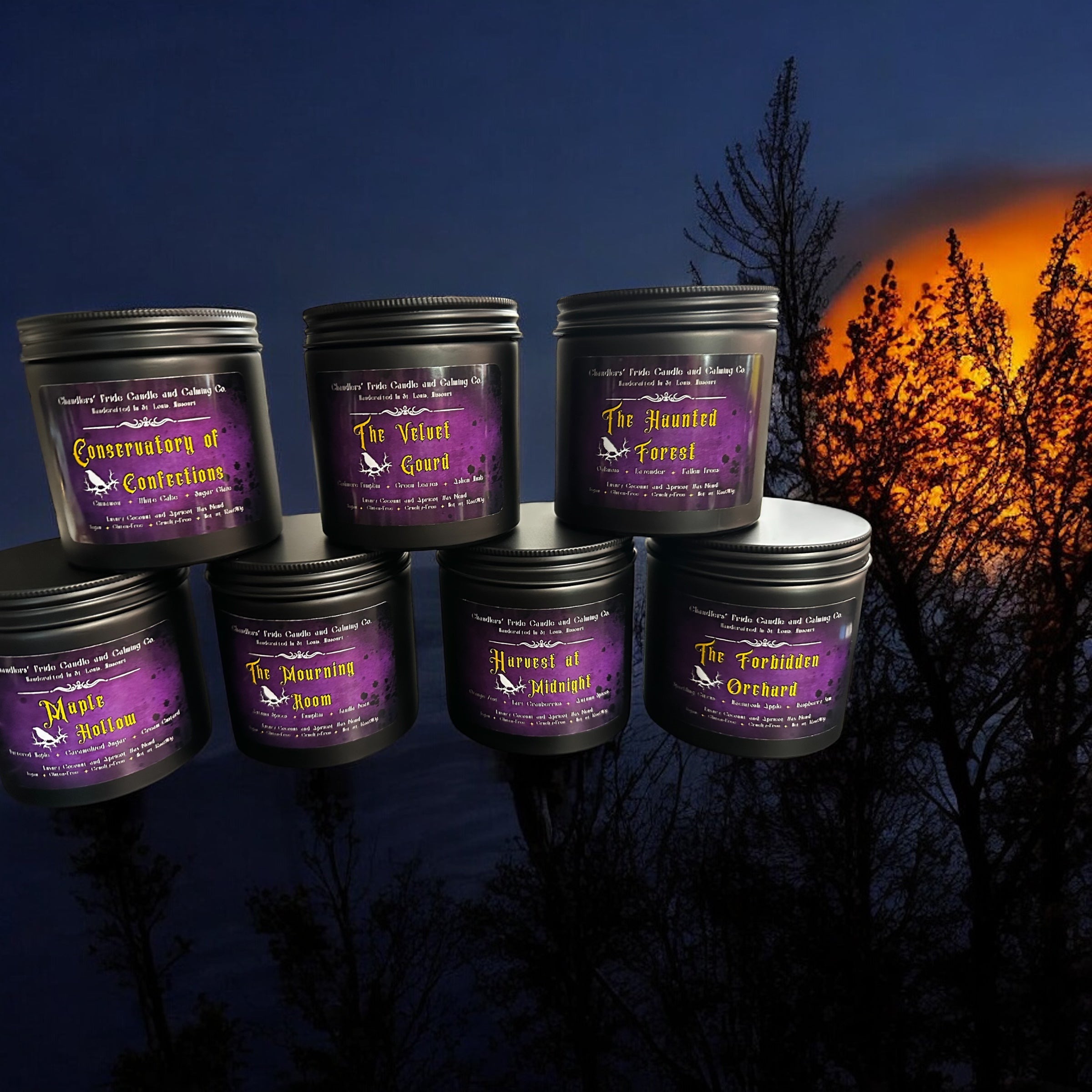Set of black candle jars with purple labels against a dark background with a sunset.